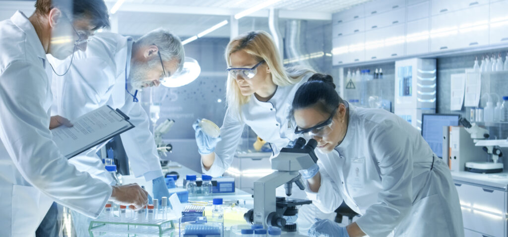 Team of Medical Research Scientists Work on a New Generation Disease Cure. They use Microscope, Test Tubes, Micropipette and Writing Down Analysis Results. Laboratory Looks Busy, Bright and Modern.