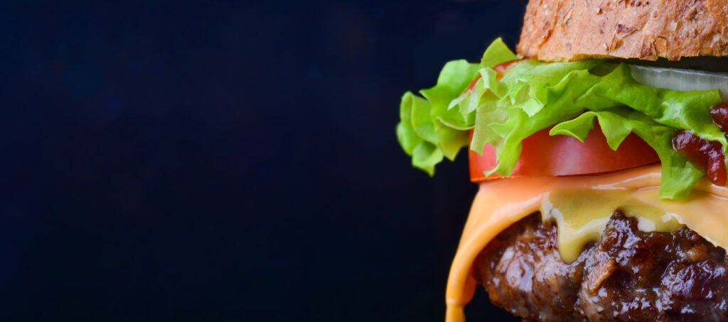 Burger flyer. Cheese burger with grilled meat, cheese, tomato, salad and onion rings. Close-up of delicious fresh home made burger with salad and cheese on bark blue background.