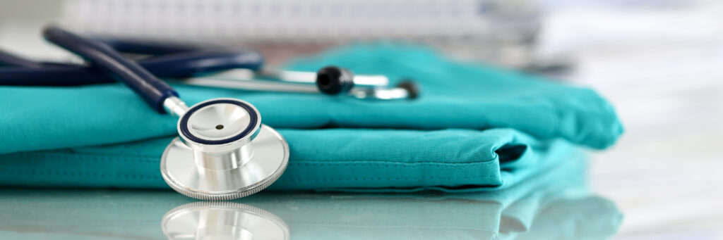 Medical stethoscope head lying on green doctor uniform in office closeup. Medical tools and instruments shop, therapeutist workspace, physical, patient examination, blood pressure measurement concept