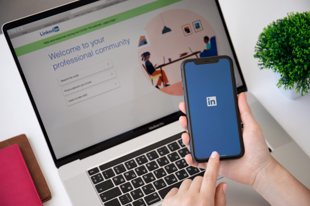 Alanya, Turkey - June 7, 2020: Woman hand holding iPhone 11 and Macbook Pro 16 with app LinkedIn in the screen.