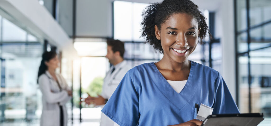 Shot of a young doctor using a digital tablet in a hospital with her colleagues in the background.