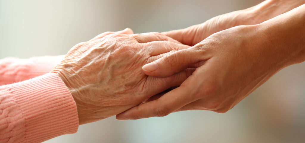 Old and young holding hands on light background, closeup